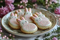 Sweet bunny sugar cookies decorated with white icing and pink details on vintage plate, surrounded by spring blossoms and rosemary sprigs for Easter celebration.