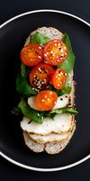 Healthy open-faced sandwich with fresh mozzarella, cherry tomatoes, spinach and sesame seeds on multigrain bread served on dark plate for breakfast or lunch.