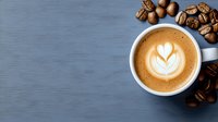 Aromatic cappuccino with heart-shaped latte art foam in white ceramic cup on blue background with scattered roasted coffee beans, top view.