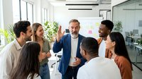 Diverse team of professionals gathered in modern office space, engaged in collaborative discussion and brainstorming session with manager leading group meeting.