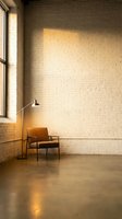 Minimalist interior with leather chair and floor lamp against white brick wall in warm sunlight streaming through large windows creating cozy atmosphere.