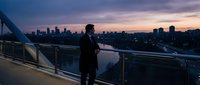Professional businessman in suit standing on modern balcony overlooking city skyline at sunset, urban lifestyle and success concept for corporate marketing.
