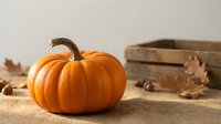 Orange pumpkin on burlap with wooden crate and autumn leaves for seasonal harvest decoration and fall holiday crafts.