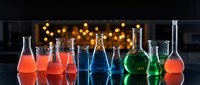 Laboratory glassware with colorful chemical solutions on reflective surface against bokeh lights background for scientific research and education.