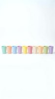 Row of colorful pastel disposable cups in mint green, peach, blue, purple, yellow, pink, cream and lime arranged on white background for party supplies.