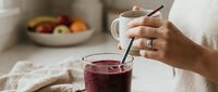 Woman pouring fresh berry juice into glass with fresh fruits in background, healthy beverage preparation for nutrition and wellness lifestyle.