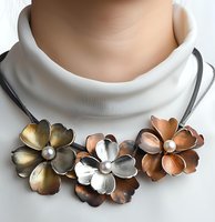 Elegant metallic flower necklace with gold, silver and copper blooms adorned with pearl centers on white leather cord. Fashion jewelry closeup.