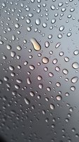 Water drops on glass surface with soft light shining through creating atmospheric mood. Macro photography showing condensation pattern on window pane.