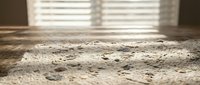 Sunlight streams through window blinds casting striped shadows on weathered concrete surface with natural texture and cracks in warm indoor setting.