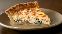 Savory quiche slice with spinach, cheese and ham in golden pastry crust on white plate, homemade brunch dish for breakfast menu and cooking recipes.
