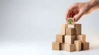 Hand placing wooden block with green plant symbol on pyramid of natural wood cubes representing sustainable business growth and eco-friendly development.