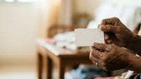 Senior African American man with dark skin holding blank white card in hands, displaying message space for text or branding in indoor home setting.