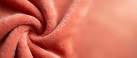 Soft coral pink fleece fabric with twisted knot detail showing cozy texture and warmth for clothing design and textile projects.