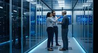 Two professional IT specialists discussing server infrastructure in modern data center with blue lighting and server racks for technology solutions.