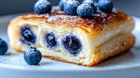 Fresh baked puff pastry filled with whole blueberries and dusted with powdered sugar, close up view showing flaky layers and juicy fruit filling.