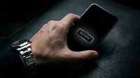Man's hand with watch holding smartphone showing buy now button on dark leather background, online shopping concept.