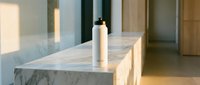 Sleek cosmetic spray bottle with minimalist design displayed on marble countertop in modern bathroom setting with natural light and contemporary architecture.