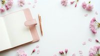 Pink leather notebook with rose gold pen surrounded by cherry blossom flowers on white background, flat lay feminine workspace.