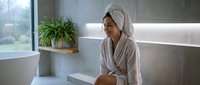 Young woman in white bathrobe and towel turban relaxing in modern spa bathroom, smiling after shower in luxury wellness retreat.