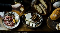 Mediterranean appetizer spread with prosciutto, cheese, olives, and crusty bread on rustic wooden table. Authentic antipasti platter for social gathering.