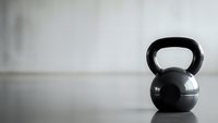 Black kettlebell on wooden floor against white wall in minimalist gym setting for strength training and fitness workouts.