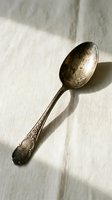 Vintage tarnished silver spoon with ornate floral pattern handle on white linen fabric creating elegant shadow for antique kitchen decor and culinary styling.