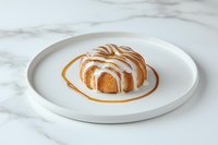 Glazed bundt cake with vanilla icing drizzle served on white ceramic plate against marble surface, fresh baked dessert for food photography and menu design.