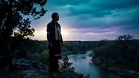 Young man silhouette standing on cliff overlooking river at sunset with dramatic sky and forest landscape for outdoor adventure and travel concepts.
