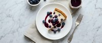 Fluffy pancakes topped with fresh blueberries and berry syrup served on white plate with marble background for breakfast menu design.