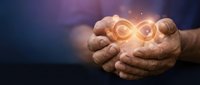 Cupped hands holding glowing infinity symbol with warm light rays and bokeh background representing endless possibilities and eternal concepts.