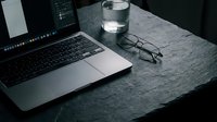 Laptop on dark stone desk with glasses and water glass, moody workspace setup for remote work, business, and productivity concepts.
