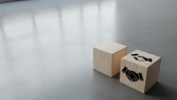 Wooden blocks with handshake and arrow symbols on concrete floor representing business partnership, teamwork and growth concepts for corporate presentations.