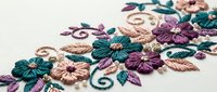 Intricate floral embroidery with teal and purple flowers, decorative swirls, and golden accents on cream fabric. Handcrafted needlework for textile design projects.