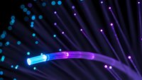 Fiber optic cable with glowing blue and purple light transmission against dark background with bokeh effects for technology and communication concepts.