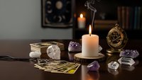 Mystical fortune telling setup with tarot cards, crystals, candles and compass on wooden table for spiritual guidance and divination practices.