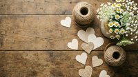 Rustic wooden background with paper hearts, twine spools and white daisy flowers for romantic crafting projects and wedding decorations.