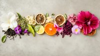 Vibrant floral arrangement with citrus slices, tropical flowers and dried botanicals creating horizontal composition on textured gray background. For wellness design.