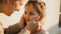 Loving grandmother gently holding granddaughter's face in tender moment of affection and care during golden hour light creating warm family bond.