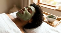 Young African American woman relaxing with green clay face mask during spa treatment at home wellness routine for skincare and self-care.