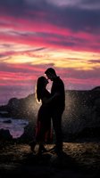 Silhouetted couple embracing at sunset with vibrant pink and golden sky, magical light particles, romantic beach scene for wedding and engagement projects.