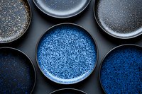 Handcrafted ceramic plates in shades of blue and black with speckled glaze pattern arranged on dark background, showcasing artisanal pottery design and texture.