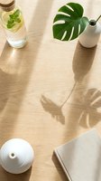 Flat lay composition with monstera leaf, infused water bottle, white ceramic vase, diffuser and linen fabric on wooden surface with natural sunlight shadows for wellness and lifestyle design projects.