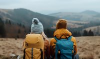 Rear view of two hikers with backpacks enjoying mountain landscape during autumn trek. Outdoor adventure and exploration in wilderness setting.