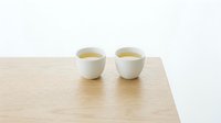 Two white ceramic tea cups filled with green tea sitting on natural wood table surface against clean white background for minimalist kitchen design.