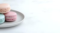 Pastel French macarons in pink, brown and mint colors arranged on white ceramic plate against light background, selective focus on sweet dessert treats.