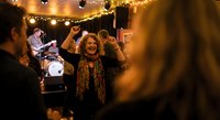 Young woman dancing joyfully at outdoor evening party with string lights and live band performing in background creating festive celebration atmosphere.
