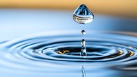 Water droplet creating ripples in calm blue surface with golden background capturing moment of impact for wellness and purity concepts.