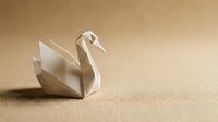 Origami paper swan on a beige textured background with copy space, showcasing the art of paper folding craft.