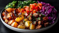 Colorful bowl with roasted potatoes, fresh tomatoes, purple cabbage and green vegetables garnished with herbs on dark background. Healthy meal concept.