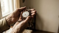 Elderly hands holding vintage pocket watch by window, representing time passage, memories, and life reflection in warm natural light.